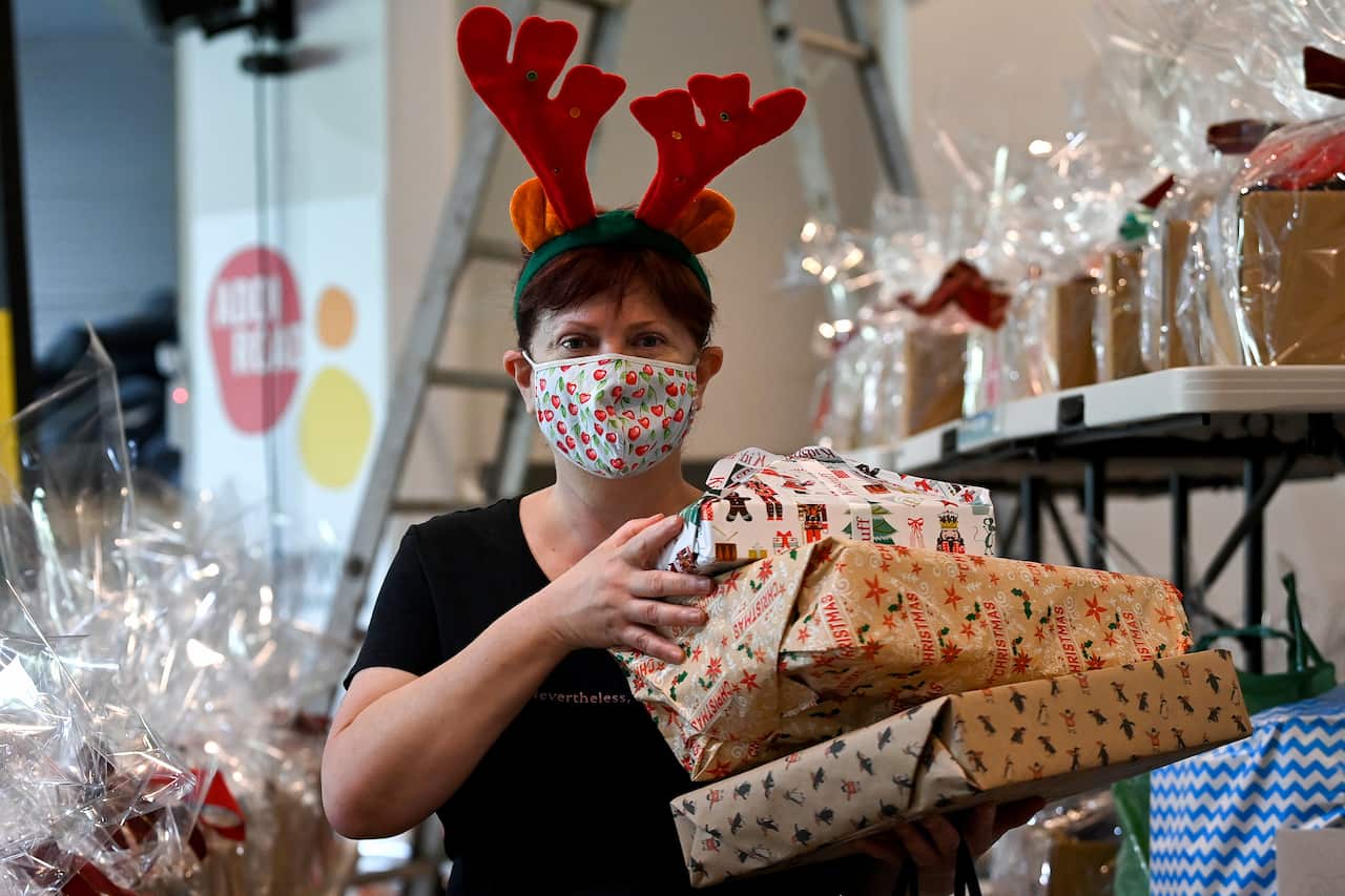 A woman wearing a festive face mask and antlers holds a pile of Christmas presents 