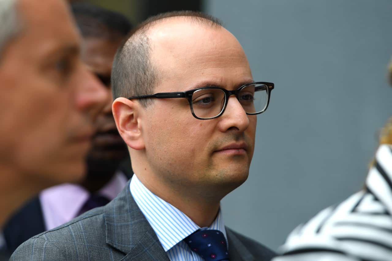 A man in black-rimmed glasses looks ahead.