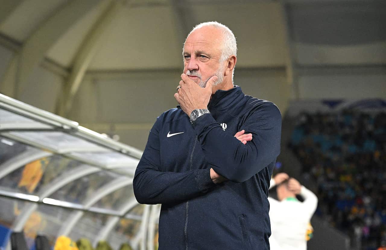 Graham Arnold wearing a dark tracksuit outside. He has his hand to his mouth