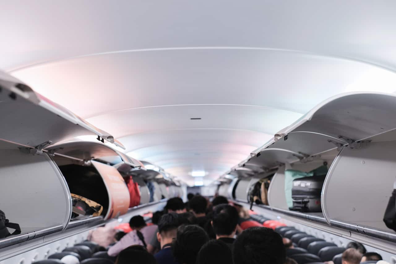 People moving through an aircraft with luggage in overhead compartments.