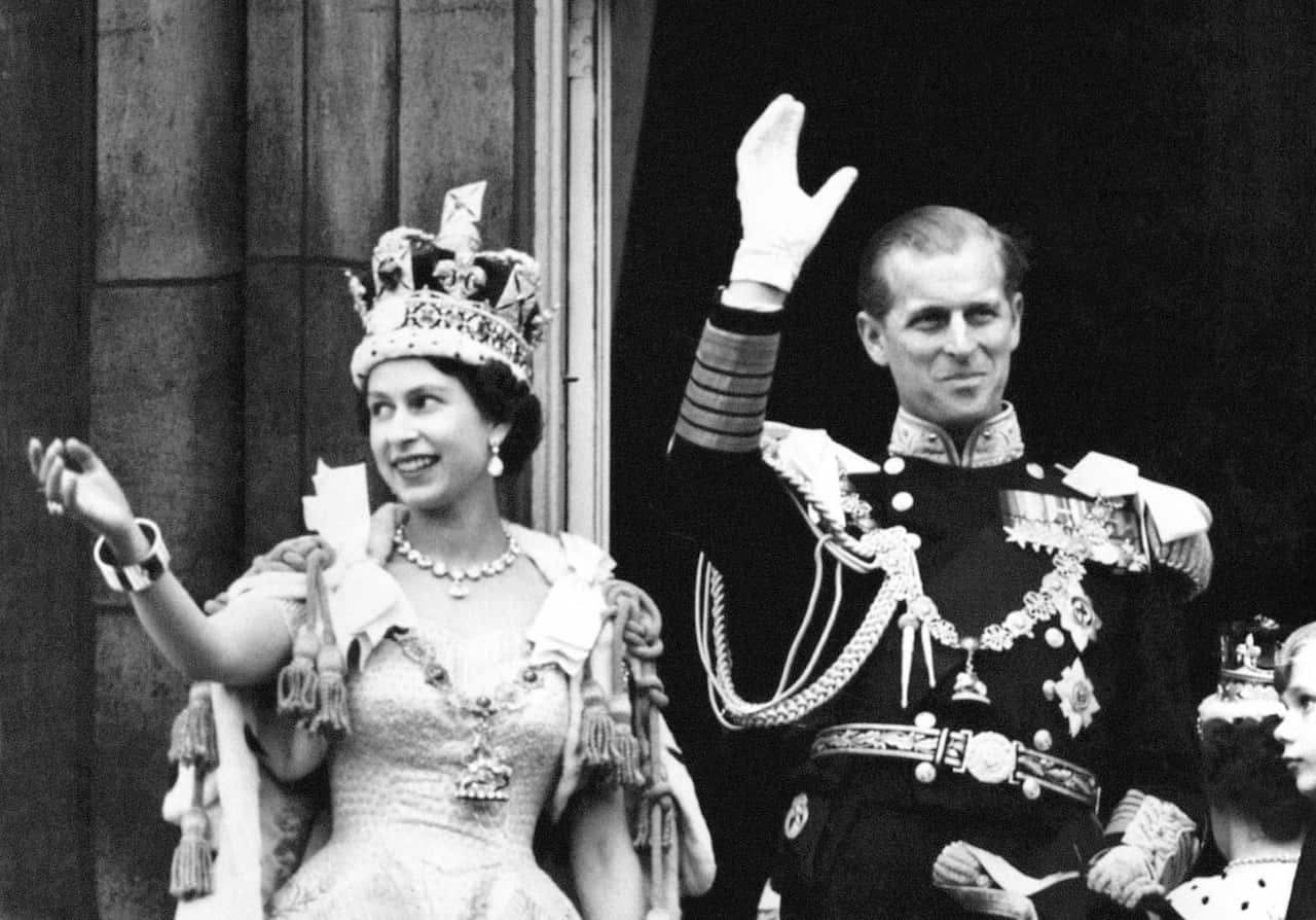 Queen Elizabeth II and the Duke of Edinburgh wave from the balcony to the onlooking crowds at the gates of Buckingham Palace after the Coronation on 2 June 1953.  