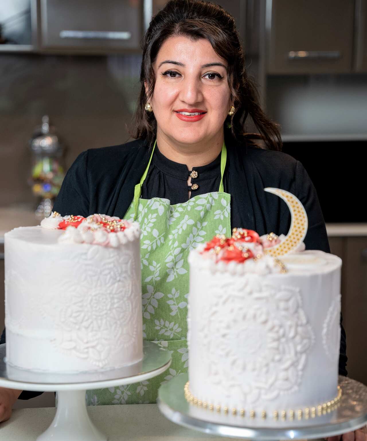 A brown haired woman stands behind a bench with two white cakes.