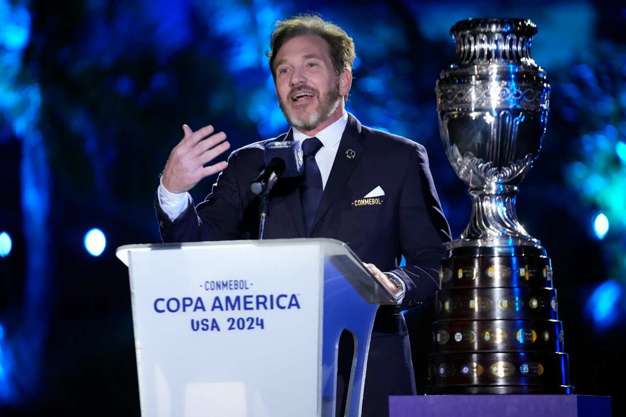 A main in a suit speaks in front of a mic.