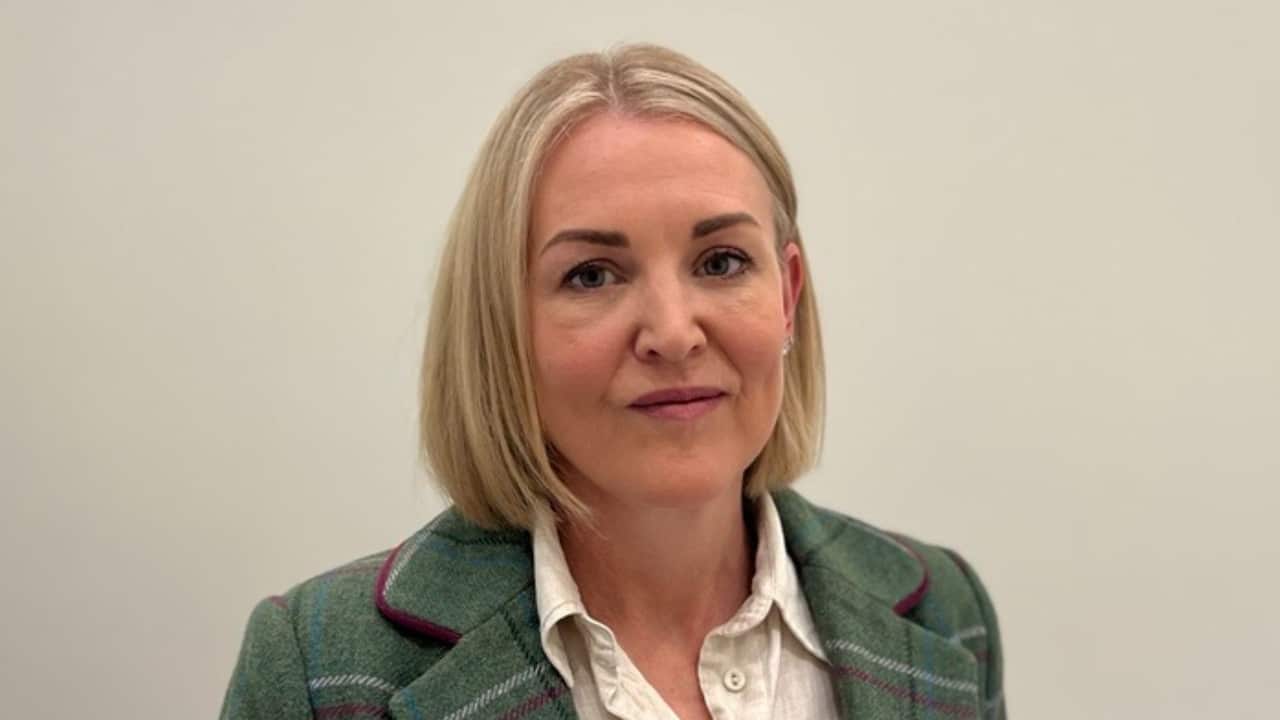 closeup shot of a middle aged woman with a blonde bob in a green tweed suit