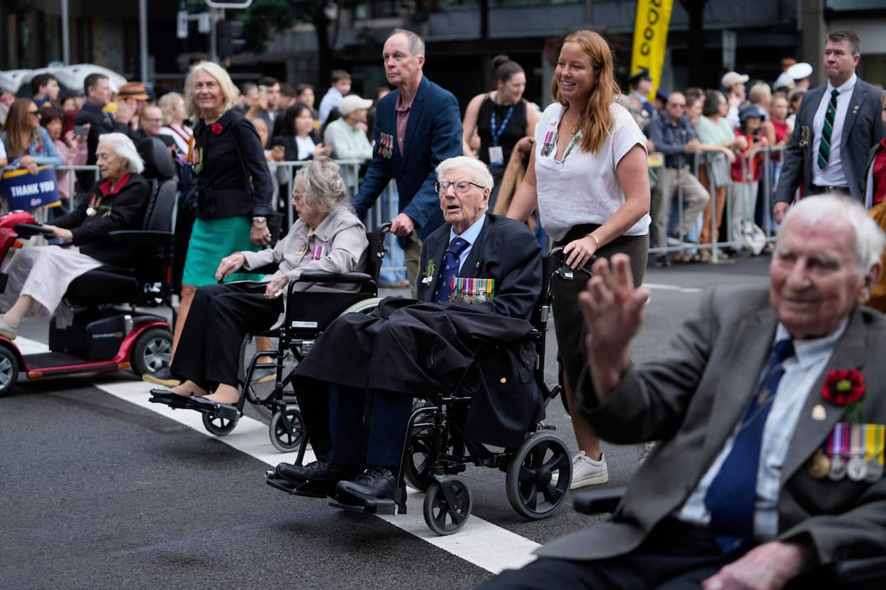 Elderly men and women in wheelchairs being walked down a blocked-off road.