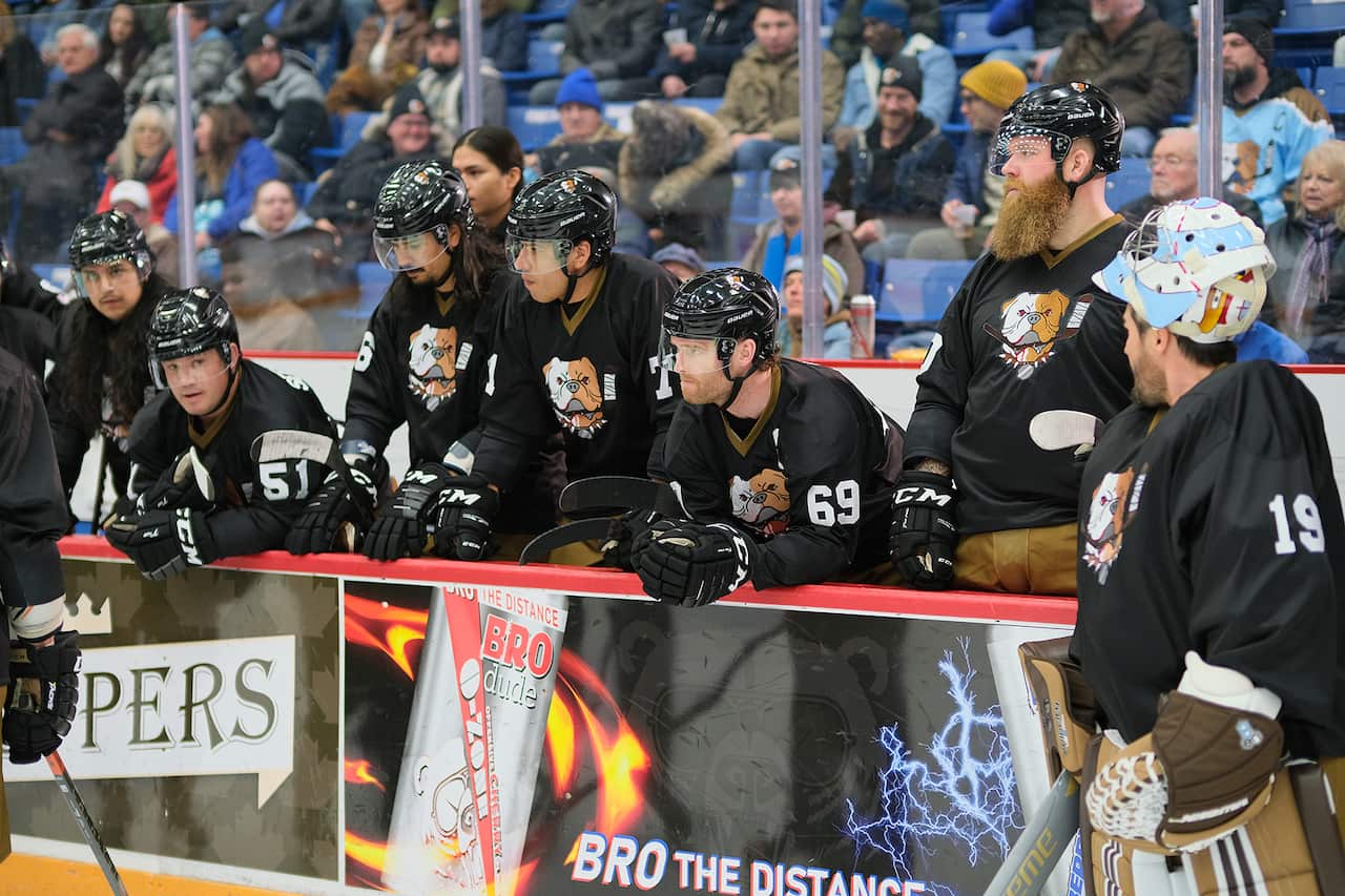 A group of ice hockey players in black uniforms line a section of the rink. 