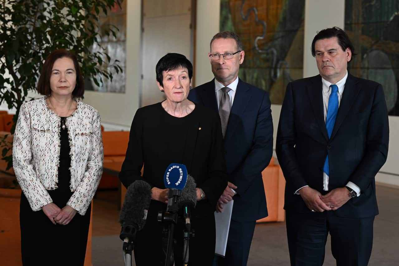 Two women and two men stand in front of microphones during a press conference