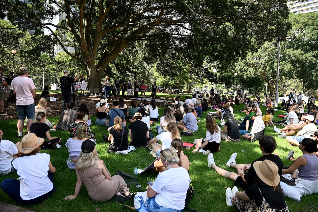 People sit outside listening to speakers at a rally. 