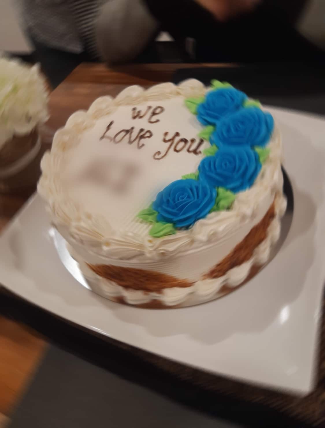 A cake with 'we love you' written on it in icing and a below a blurred name.
