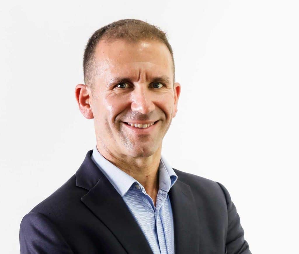 A man in a grey suit and blue shirt smiling