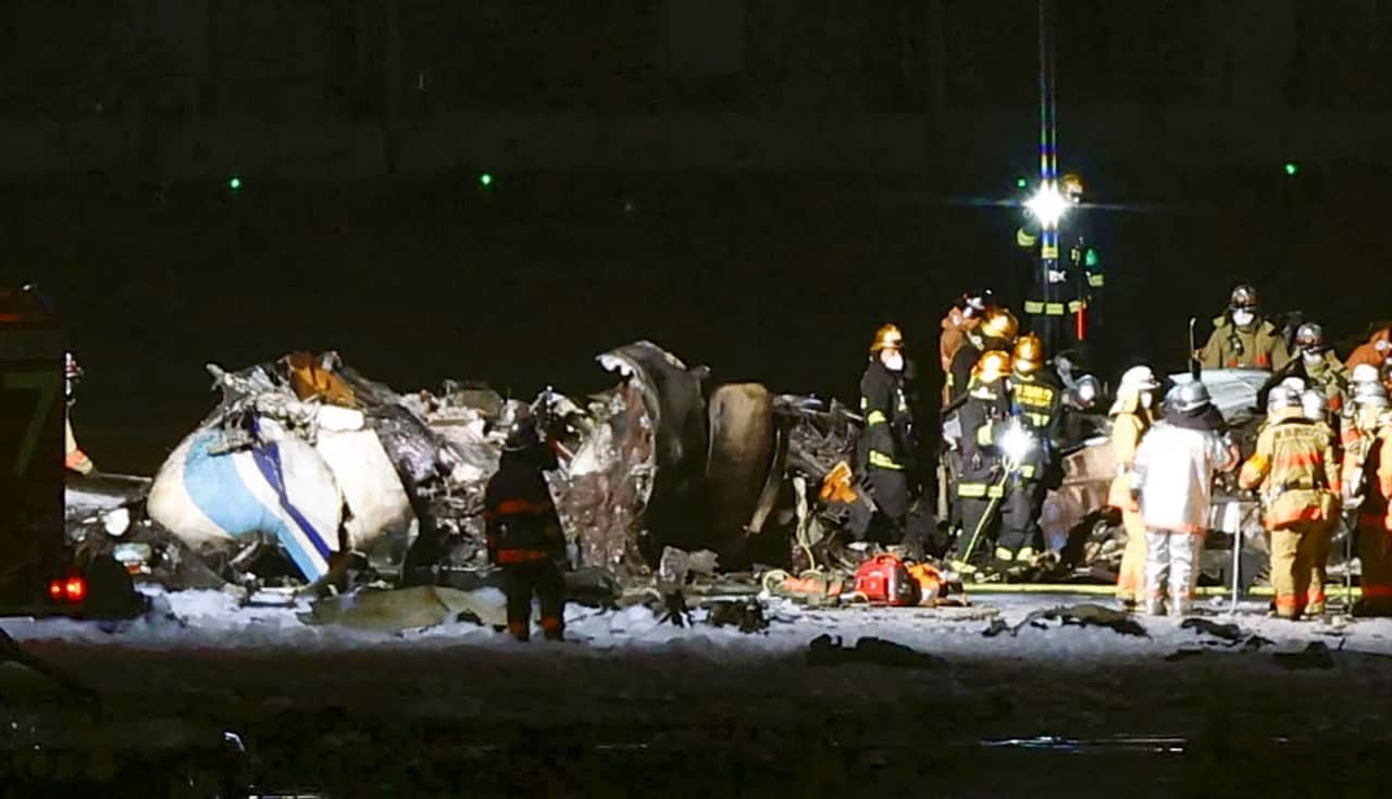 Firefighters are seen near the part of the burnt Japanese Coast Guard aircraft on the runway of Haneda airport.