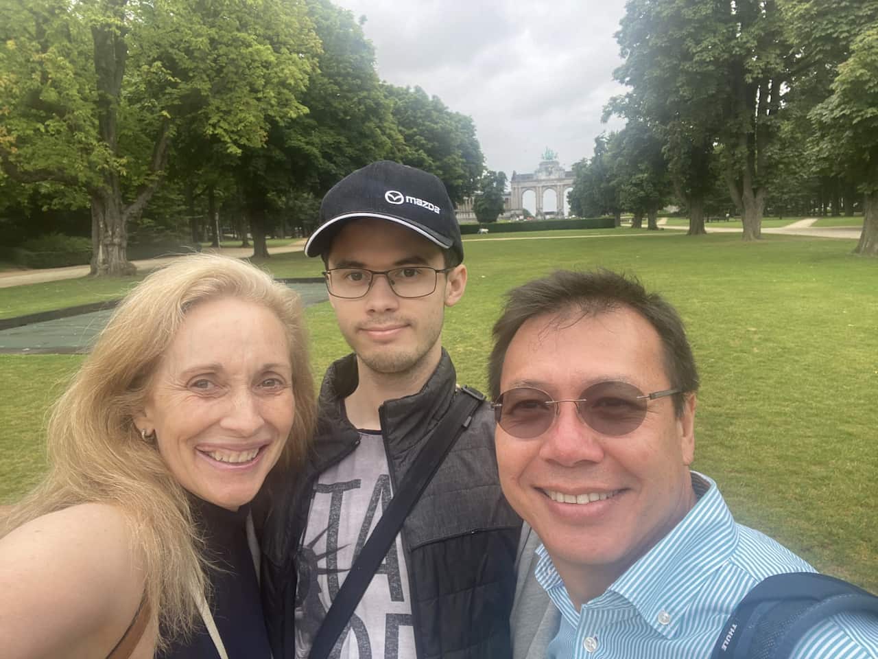 A woman smiles next to a younger man in a hat and an older man wearing sunglasses. 