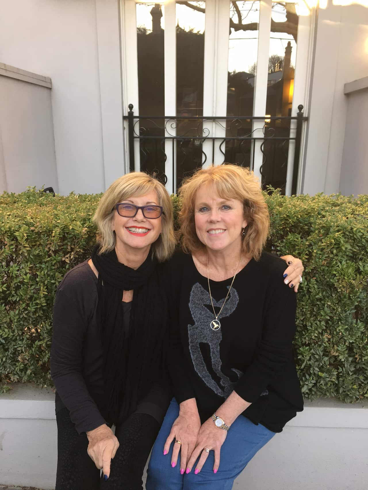 Two women sitting together outside on a garden ledge and posing for a photograph