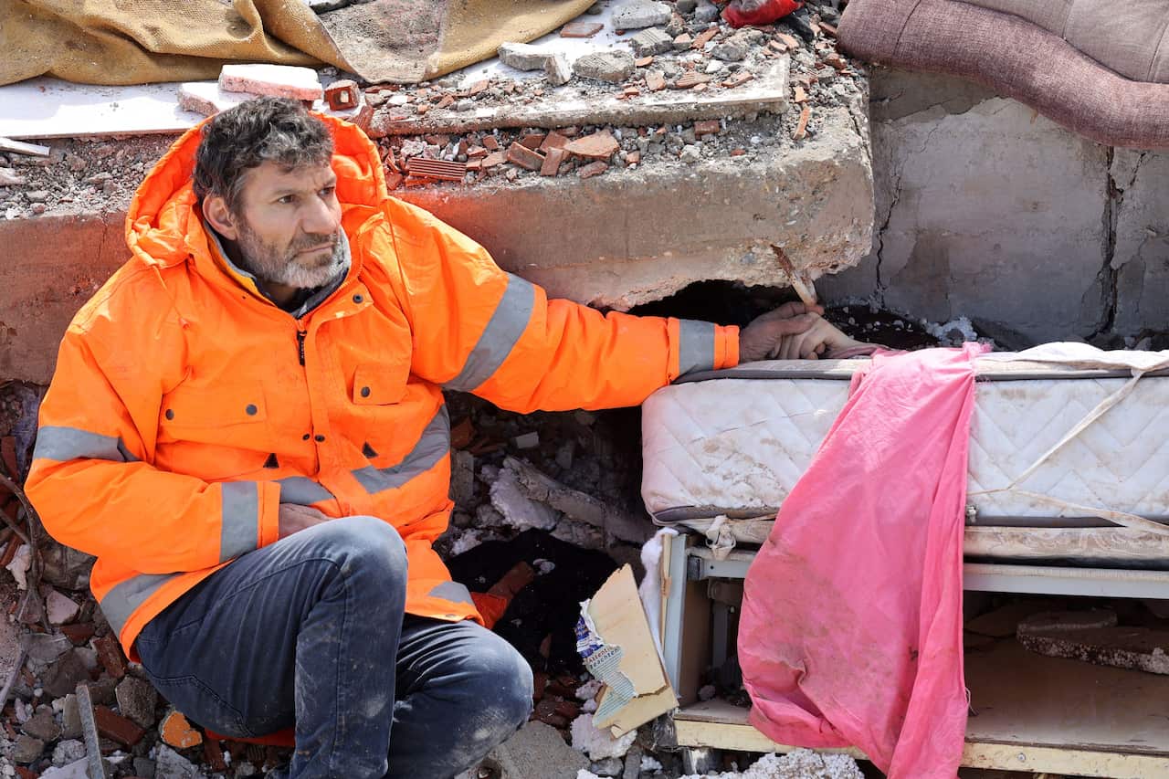 A man sitting down and holding the hand of someone who is beneath rubble. 