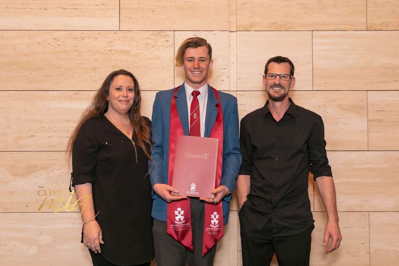 Brayden holds his high school year book as he stands next to his parents at his graduation ceremony.