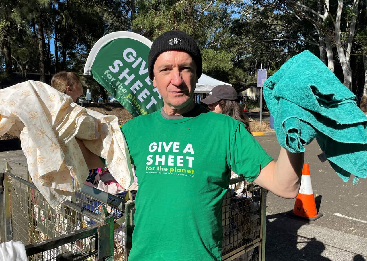 Adrian Jones holding up sheets and towels at a textile collection event in Syney.