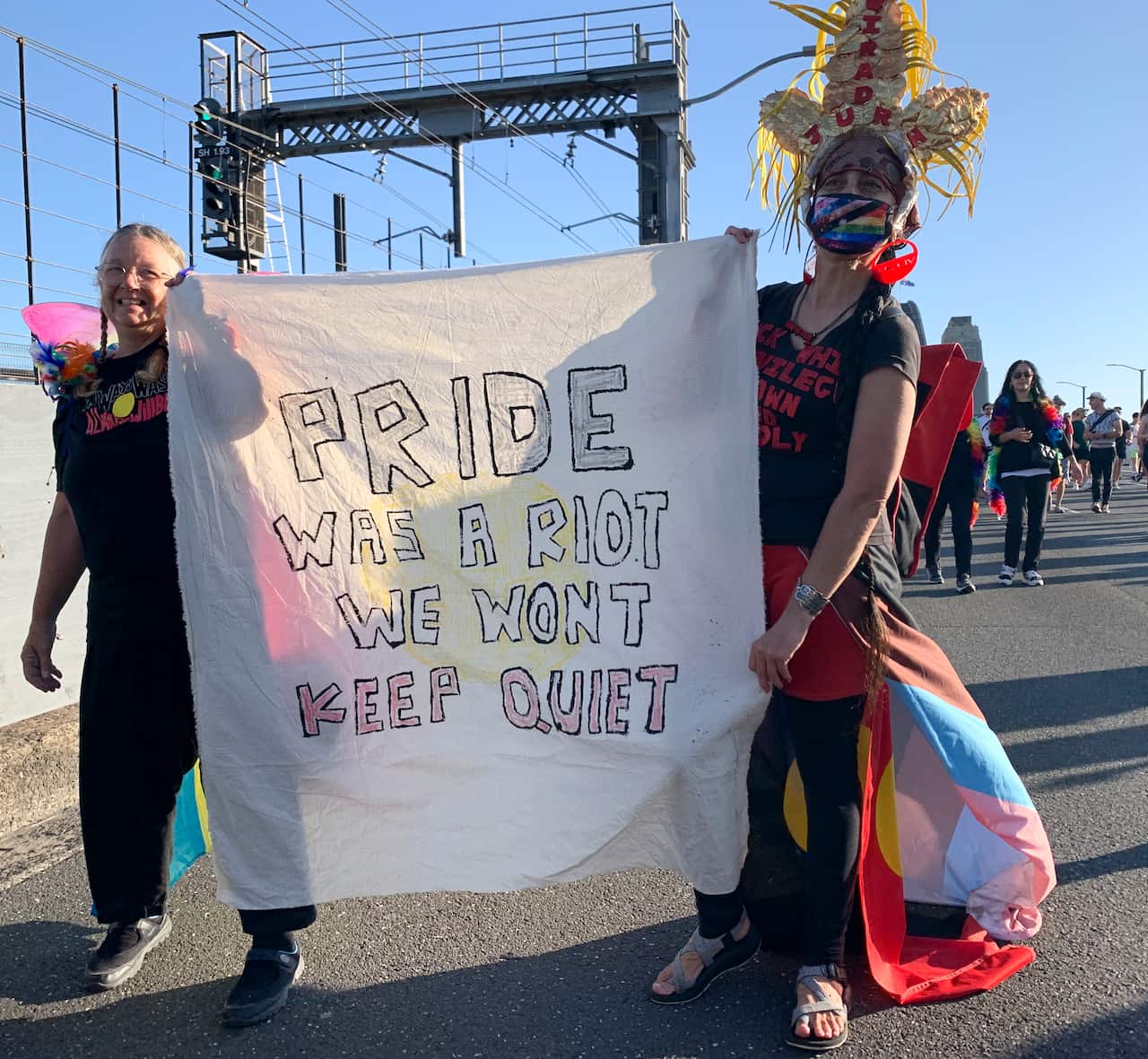 Two activists holding a sign: Pride was a riot, we won't keep quiet