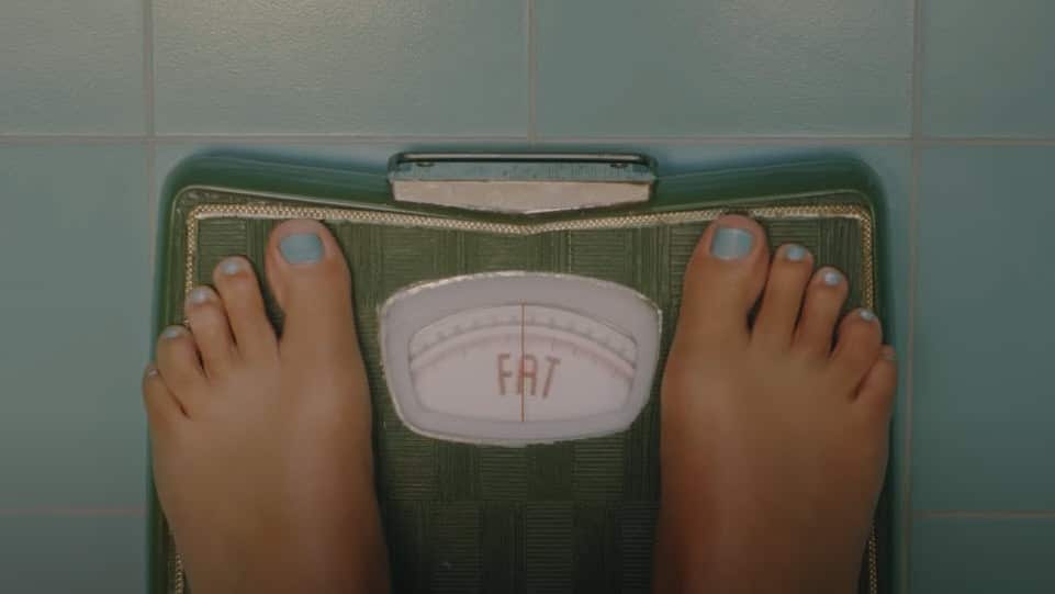 A pair of feet on scales with the word 'fat' written in red capital letters