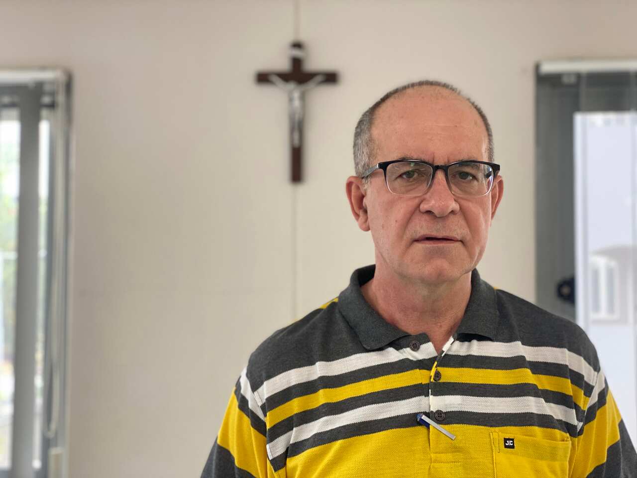 Father Giorgio Licini wearing a polo shirt. There is a crucifix on the wall behind him