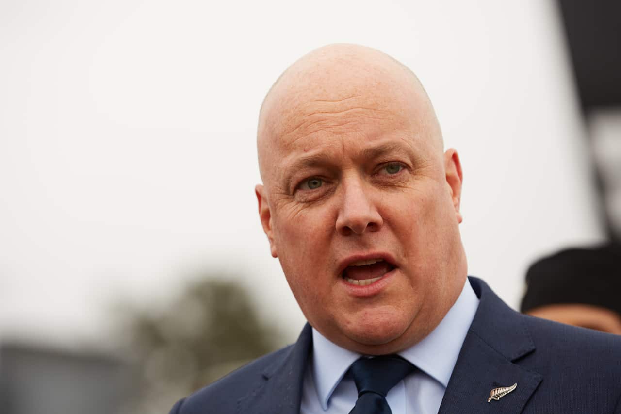 A man speaking, wearing a blazer with a silver fern pin.