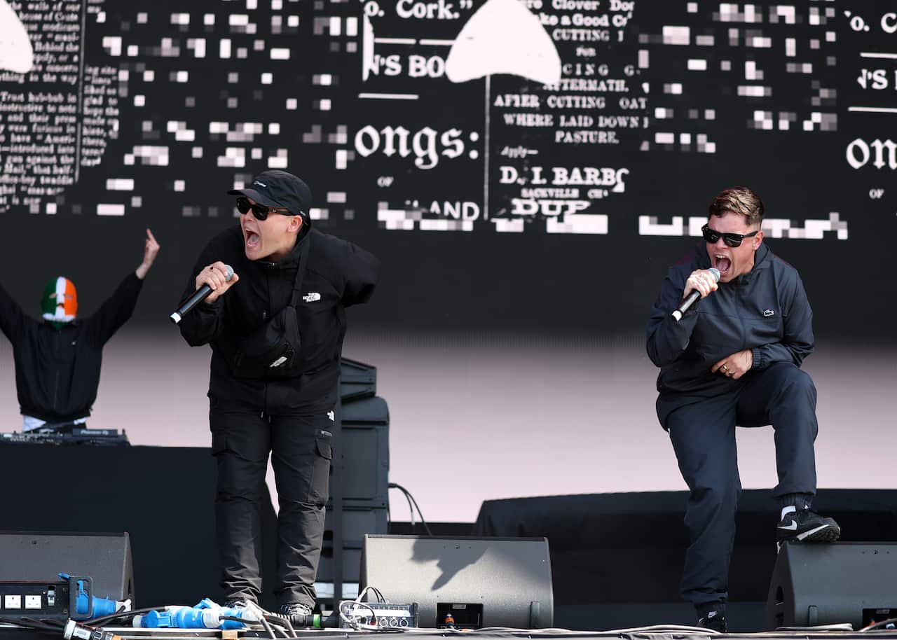 Two men dressed in black on a stage sing into microphones