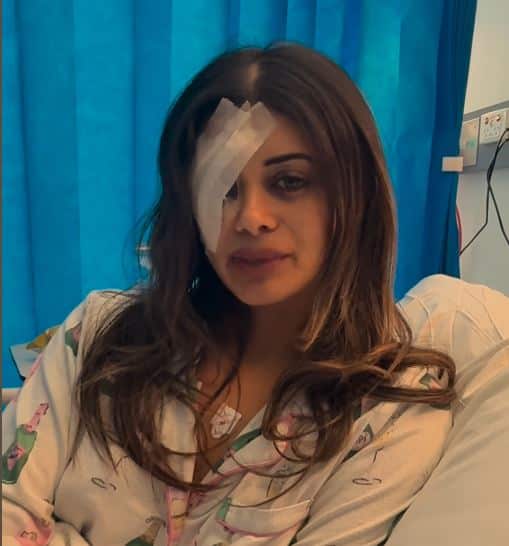 A woman is in a hospital bed with her right eye covered with gauze.