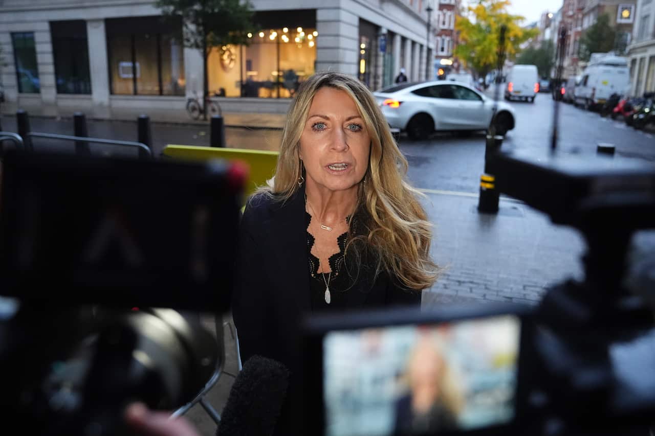 A woman facing news cameras on a street