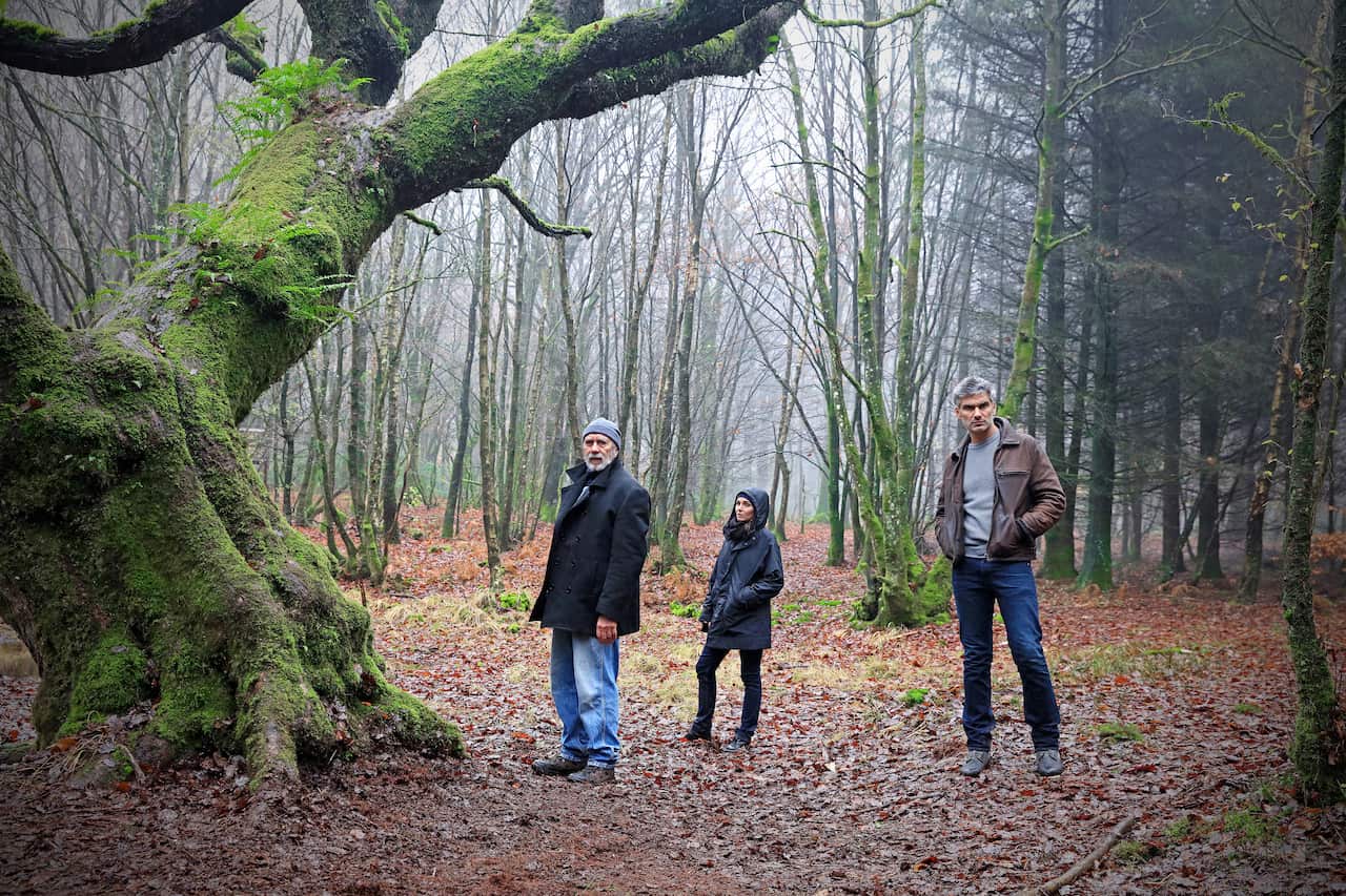 Two men and a woman stand in the cold French woods