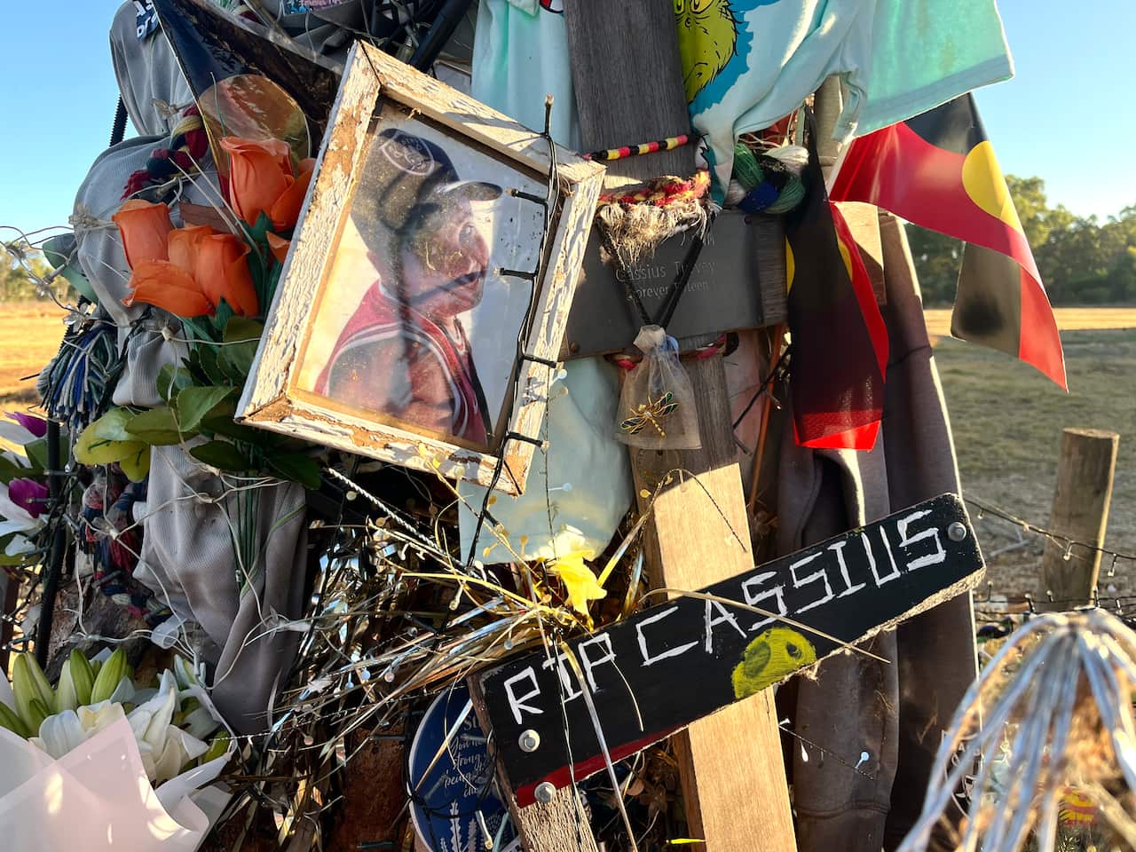 A memorial of photos, flowers and flags that says 'RIP Cassius."