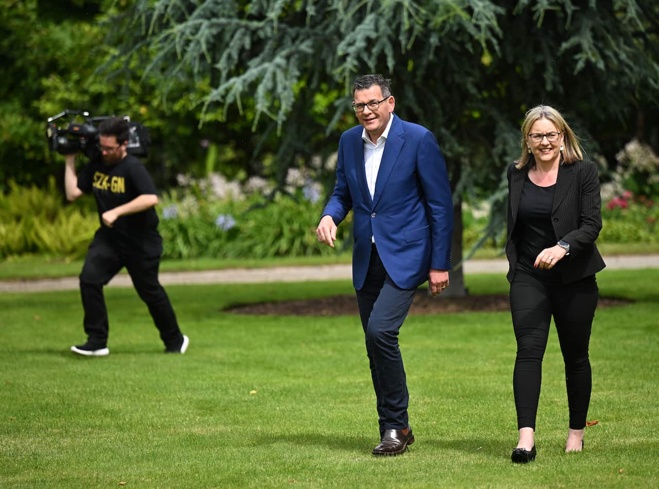 Dan Andrews and his deputy Jacinta Allan  walk on grass with a camera operator behind them