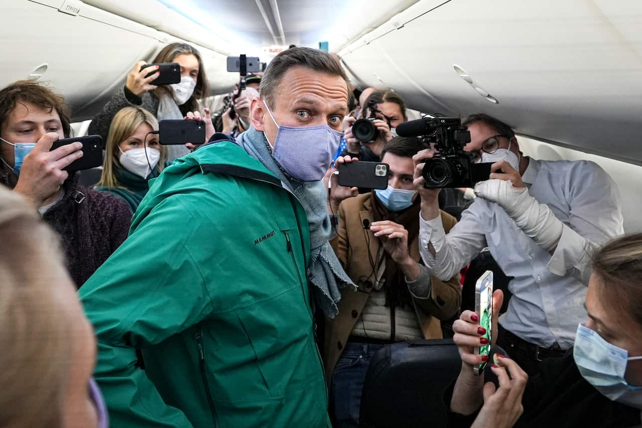 Alexey Navalny on a plane wearing a face mask with journalists surrounding him.