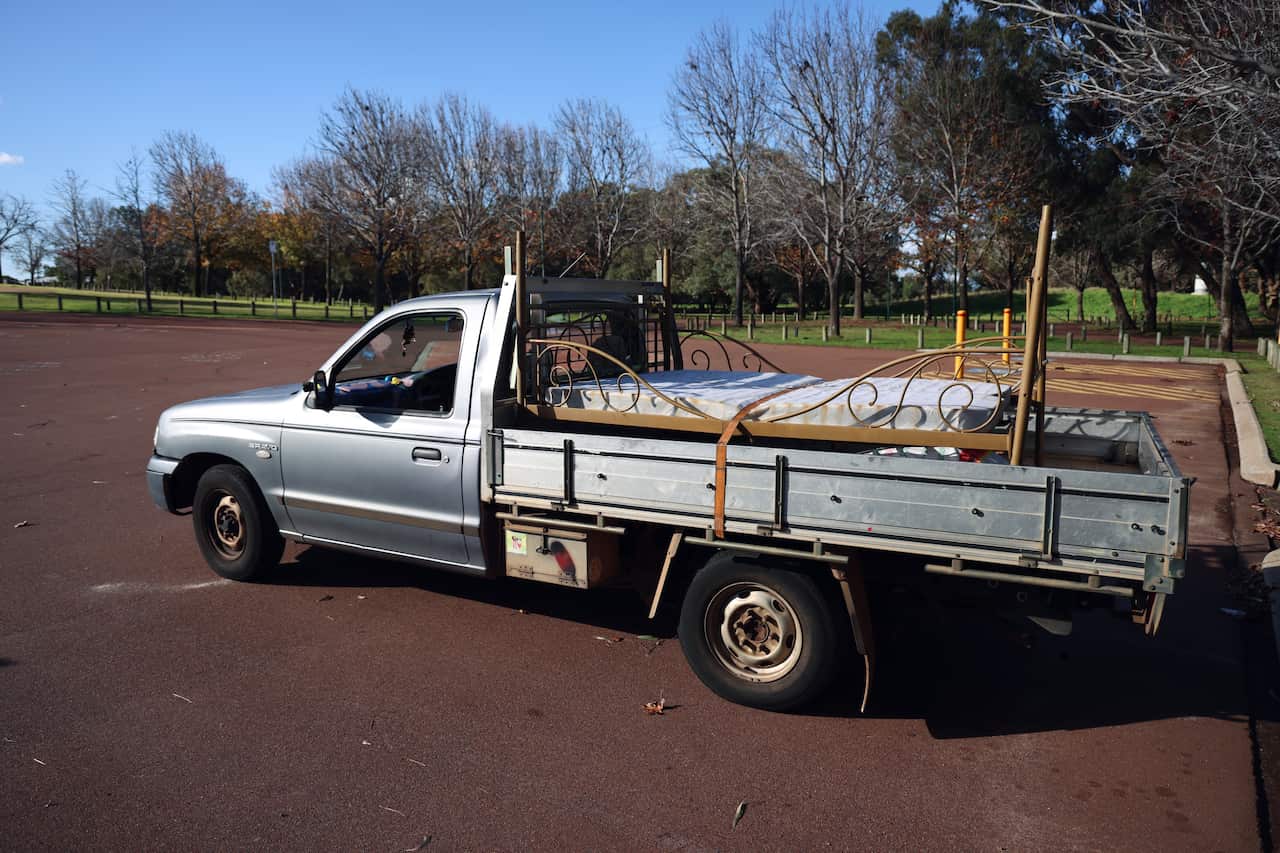 A blueish silver single cab ute parked in a car park, with a bed loaded at the back of the tray.