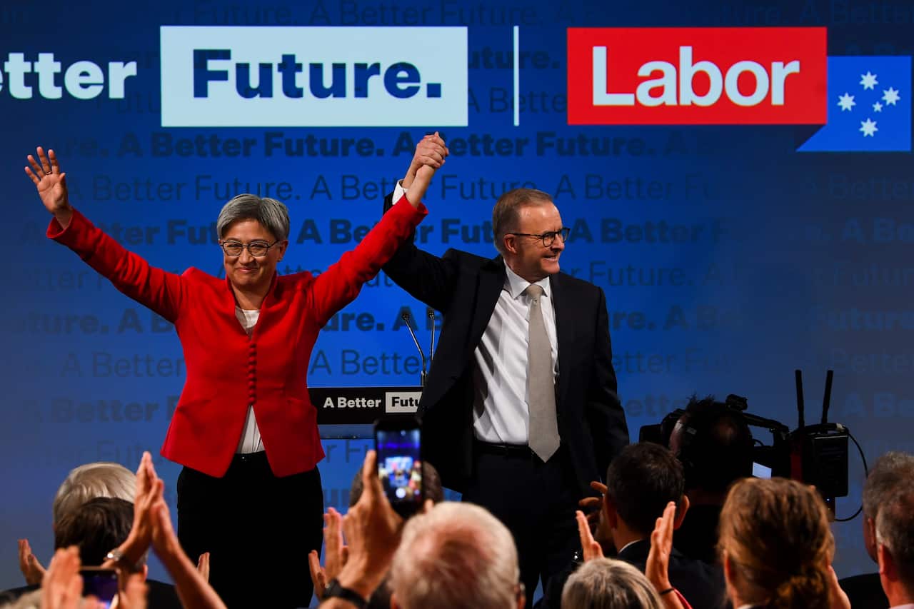 An Asian woman and white man stand on a stage with their arms in the air.