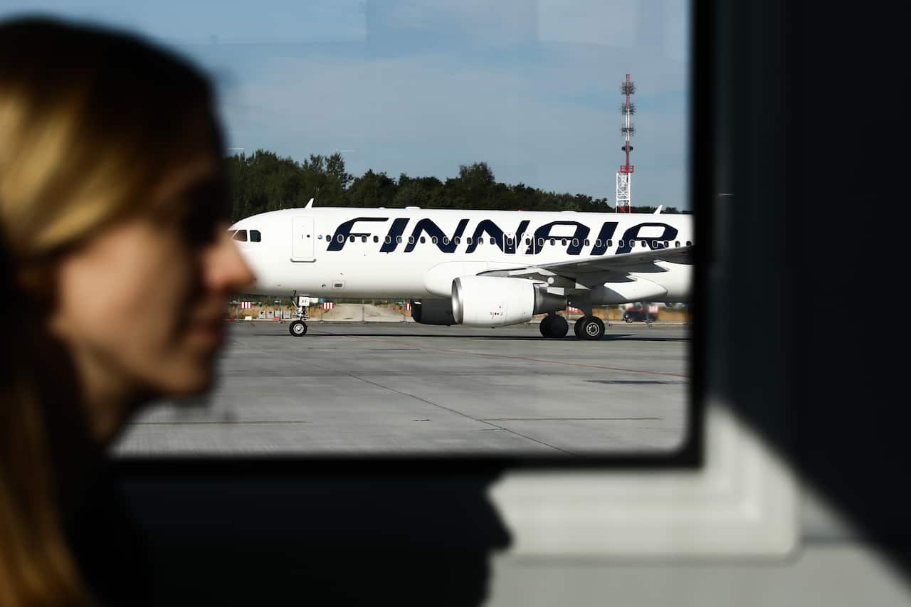 A passenger waiting in a departure lounge. Outside the window is a plane with a "Finnair" logo.