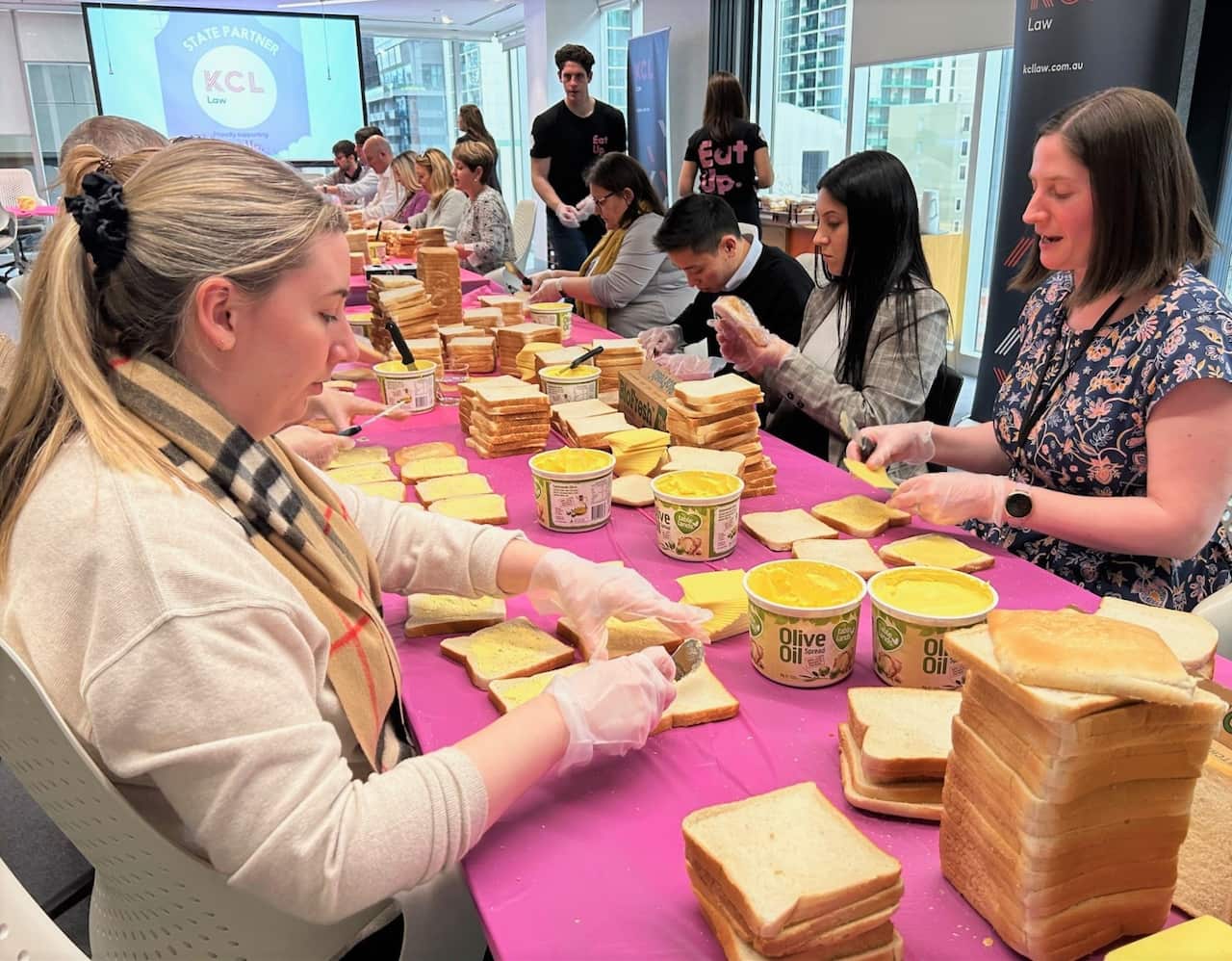 People sit at a large table making sandwiches.