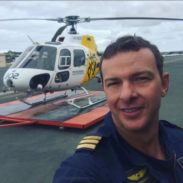 A man taking a selfie. A helicopter is behind him.