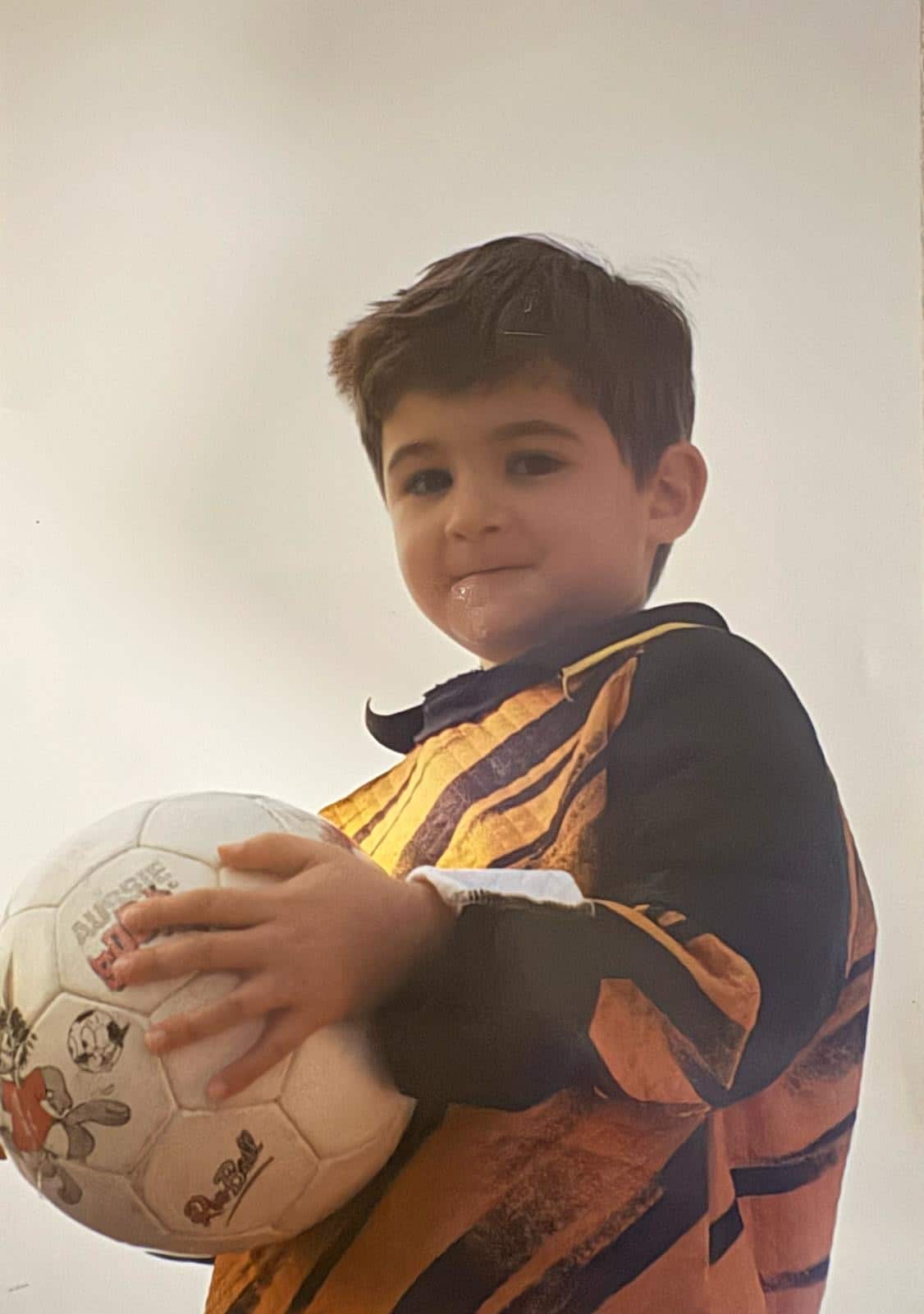 A boy wearing a football jersey is holding a soccer ball 