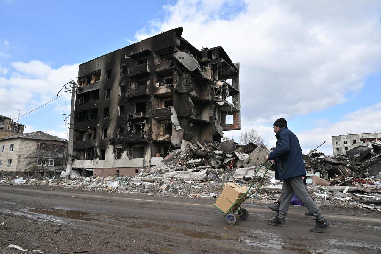 People are seen walking past destroyed buildings.