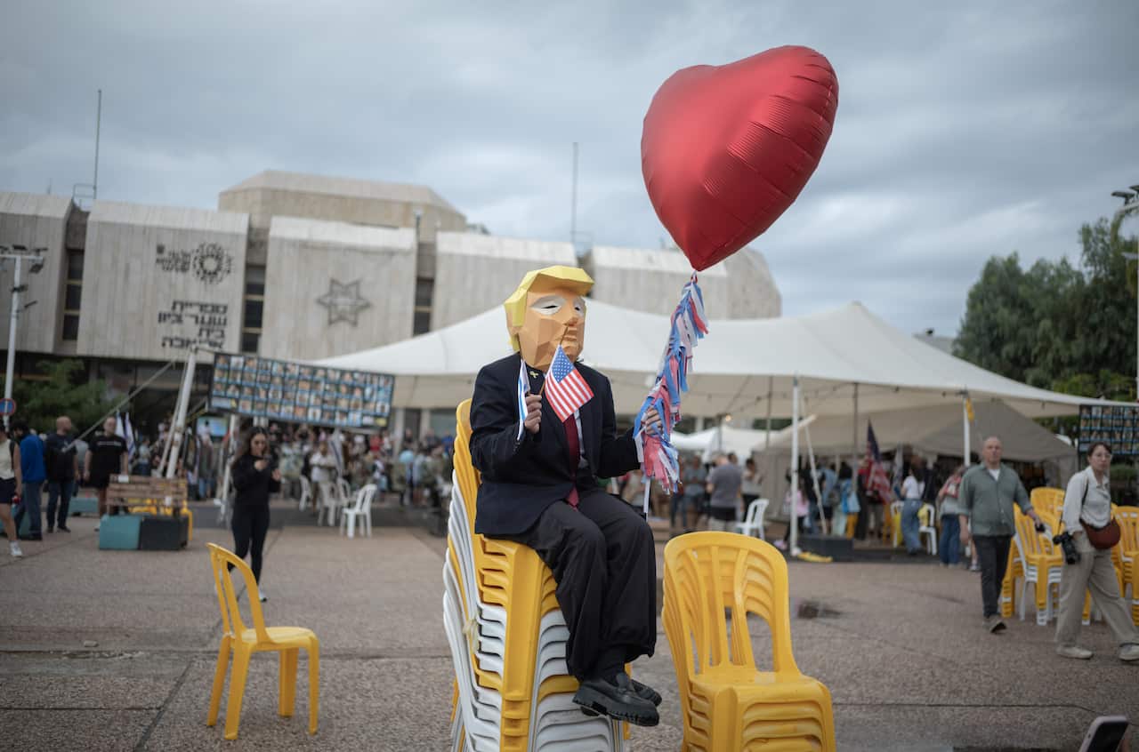 A person wearing a mask resembling Donald Trump sitting on a stack of plastics chairs.