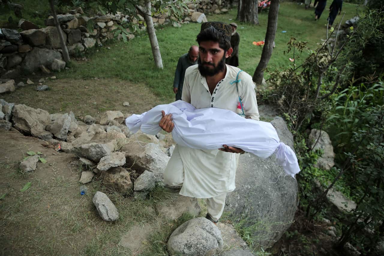 A man in a cream-coloured traditional outfit holding the body of a child wrapped in a white shroud.