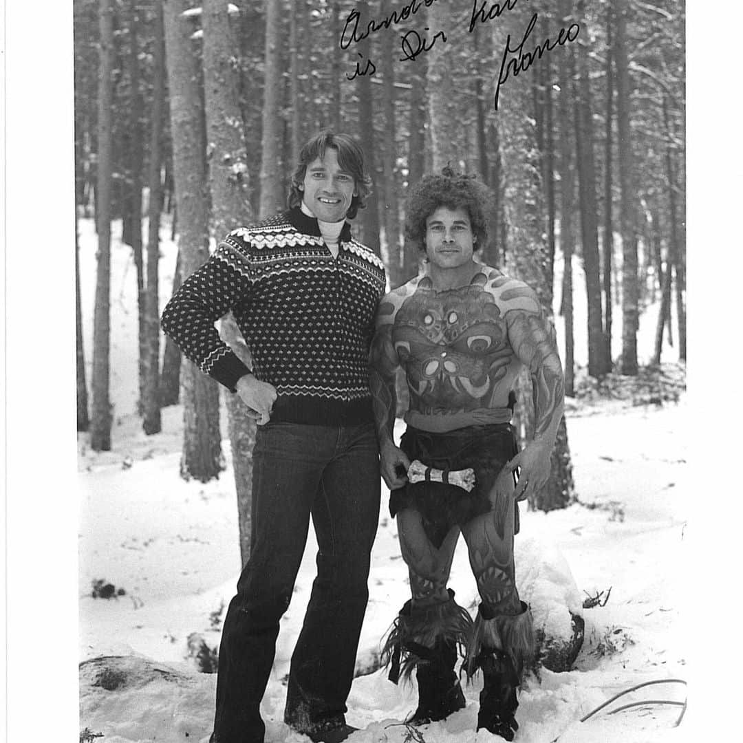 Black and white picture of Arnold Schwarzenegger (left) and Franco Columbu. They are standing in a forest and there is snow on the ground.