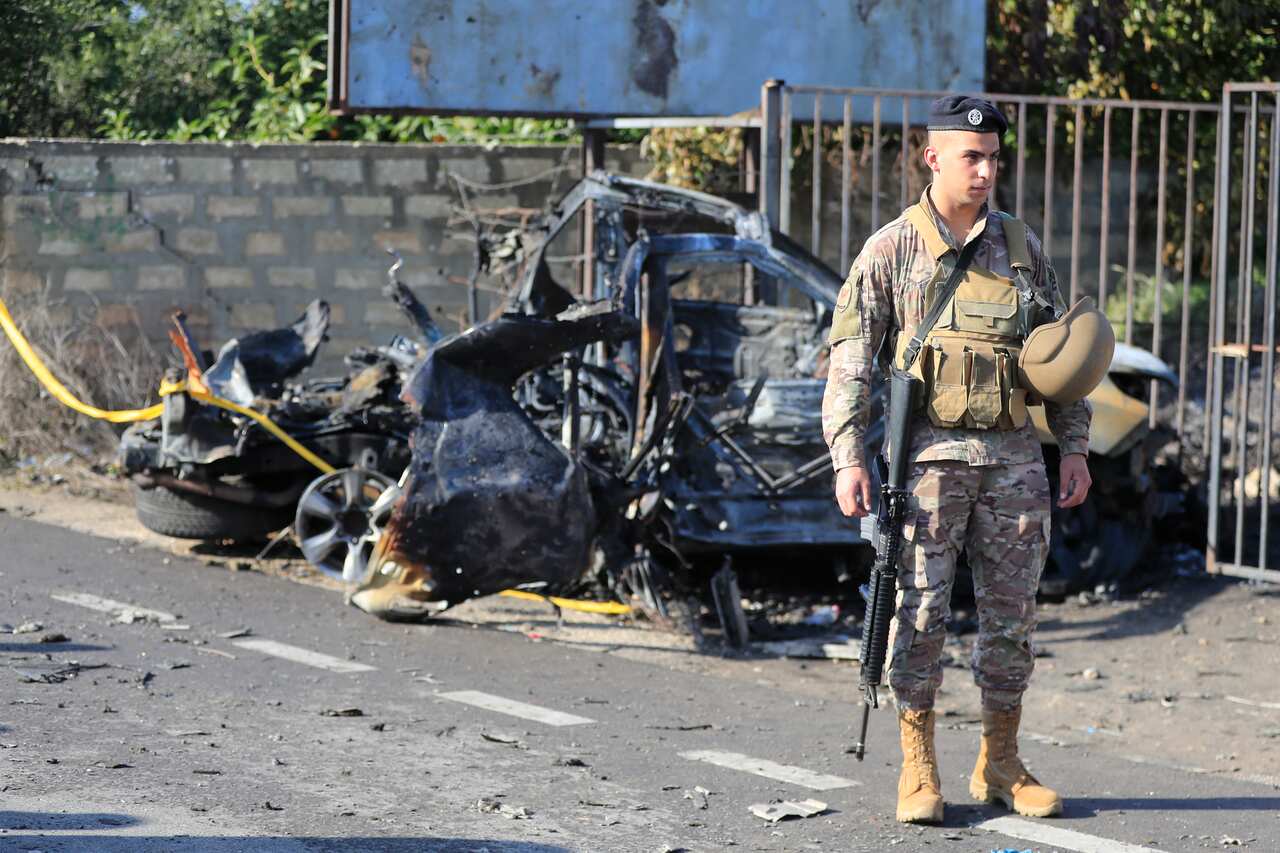 A soldier standing in front of a destroyed car.