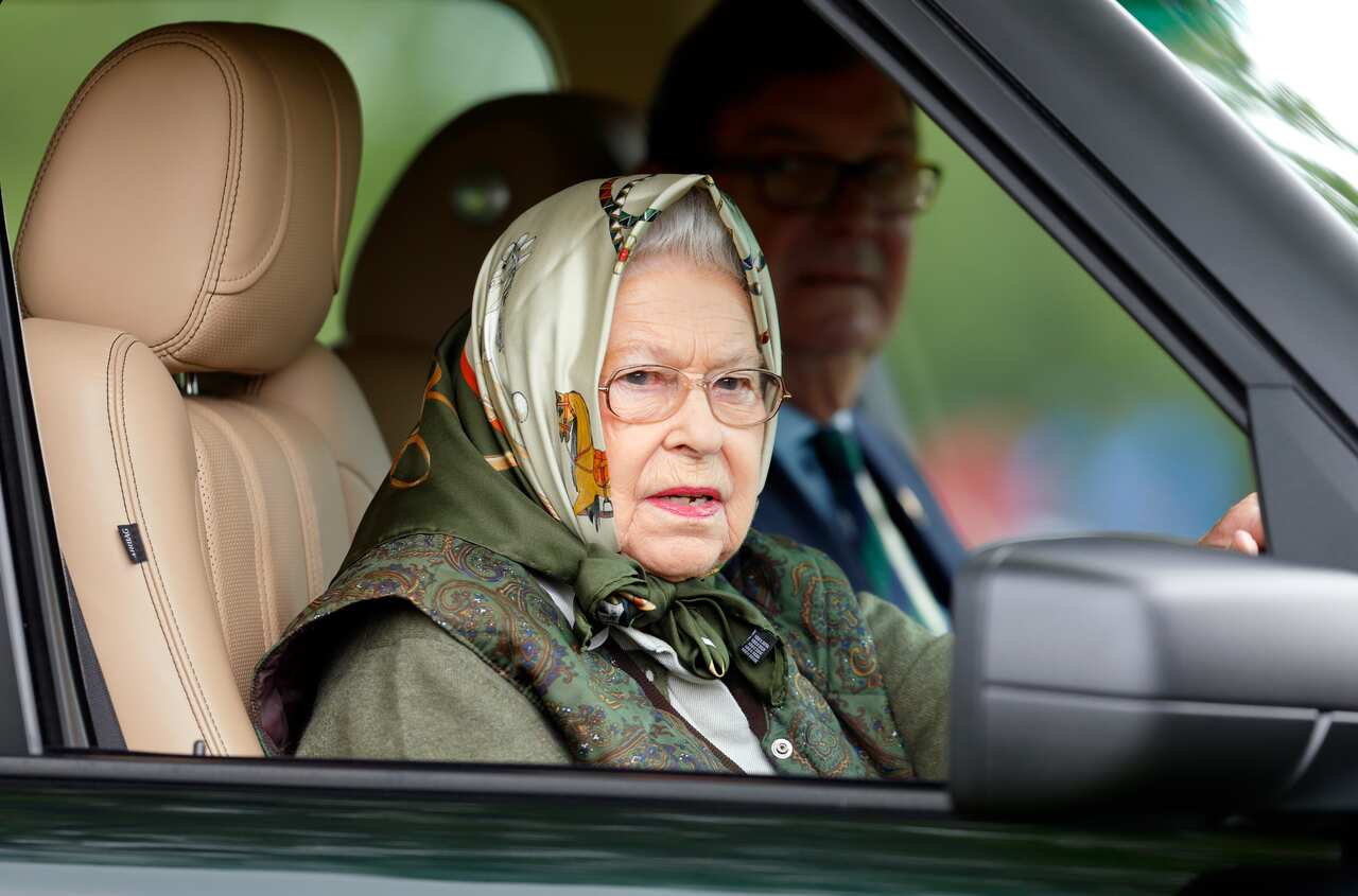 An older woman in a headscarf drives a car.