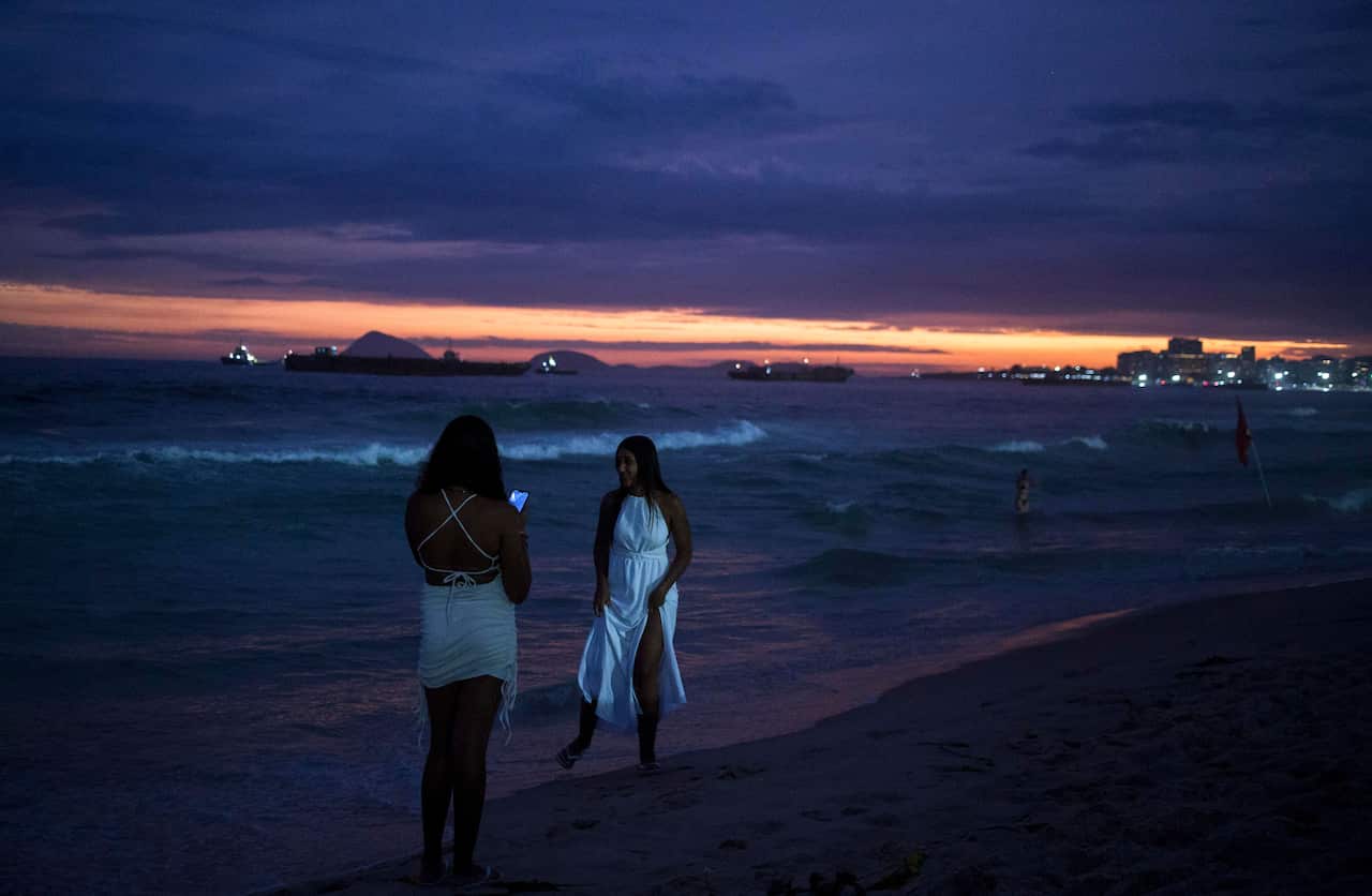 Two girls wearing white clothes standing on a beach.