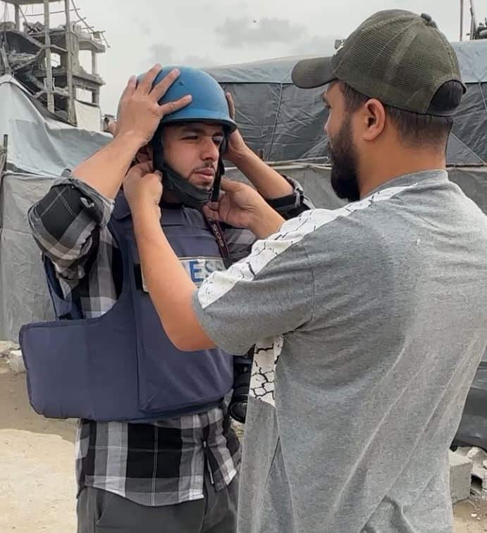 A man adjusts a blue helment on the head of a journalist.