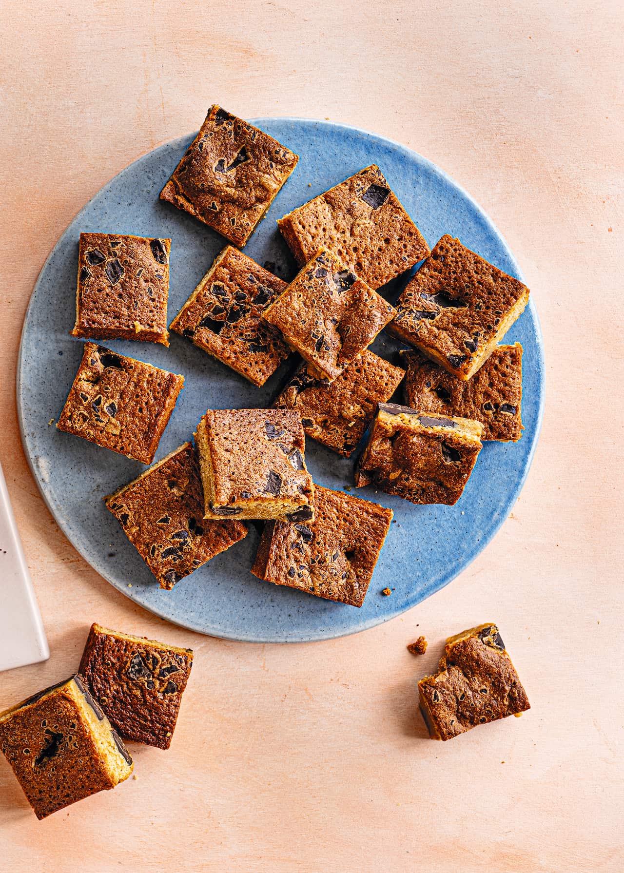 Blondie squares, studded with dark chocolate, sit on a blue plate. 