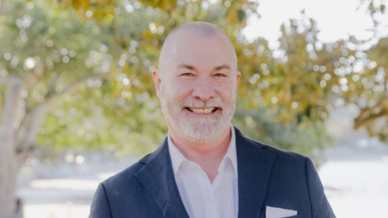 a closeup photo of a middle aged man with a shaved head in a garden