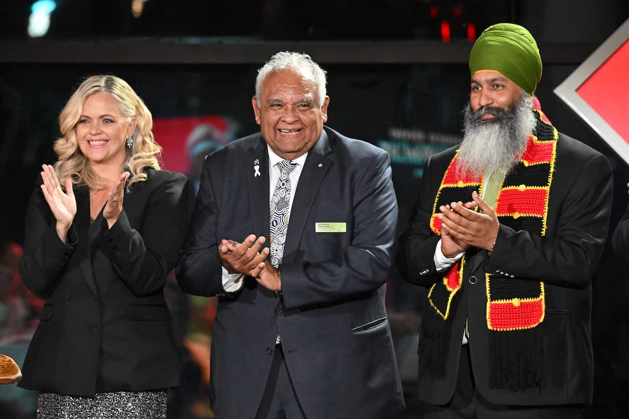 A woman and two men clapping while standing on a stage.