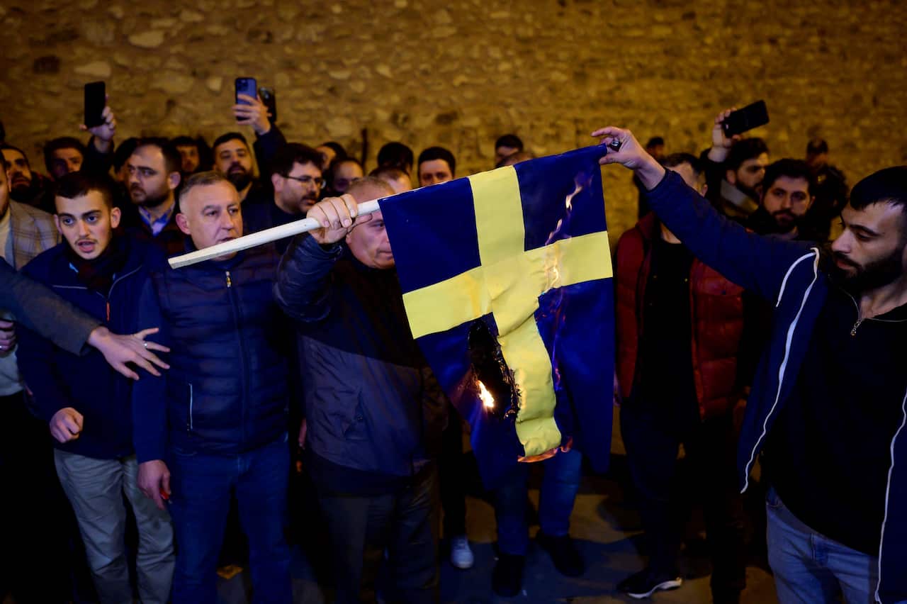 People hold up a Swedish flag which is burning
