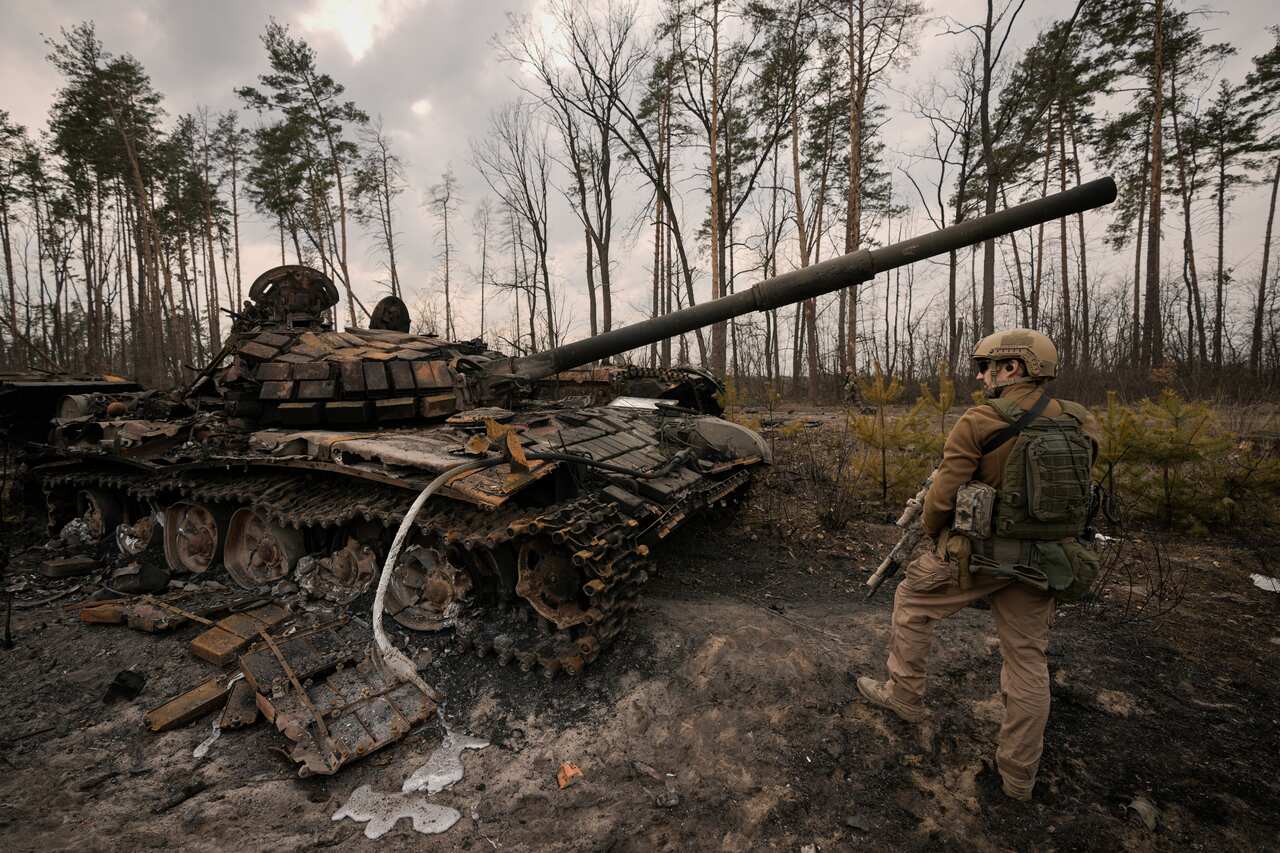 A Ukrainian serviceman stands next to a destroyed Russian tank.